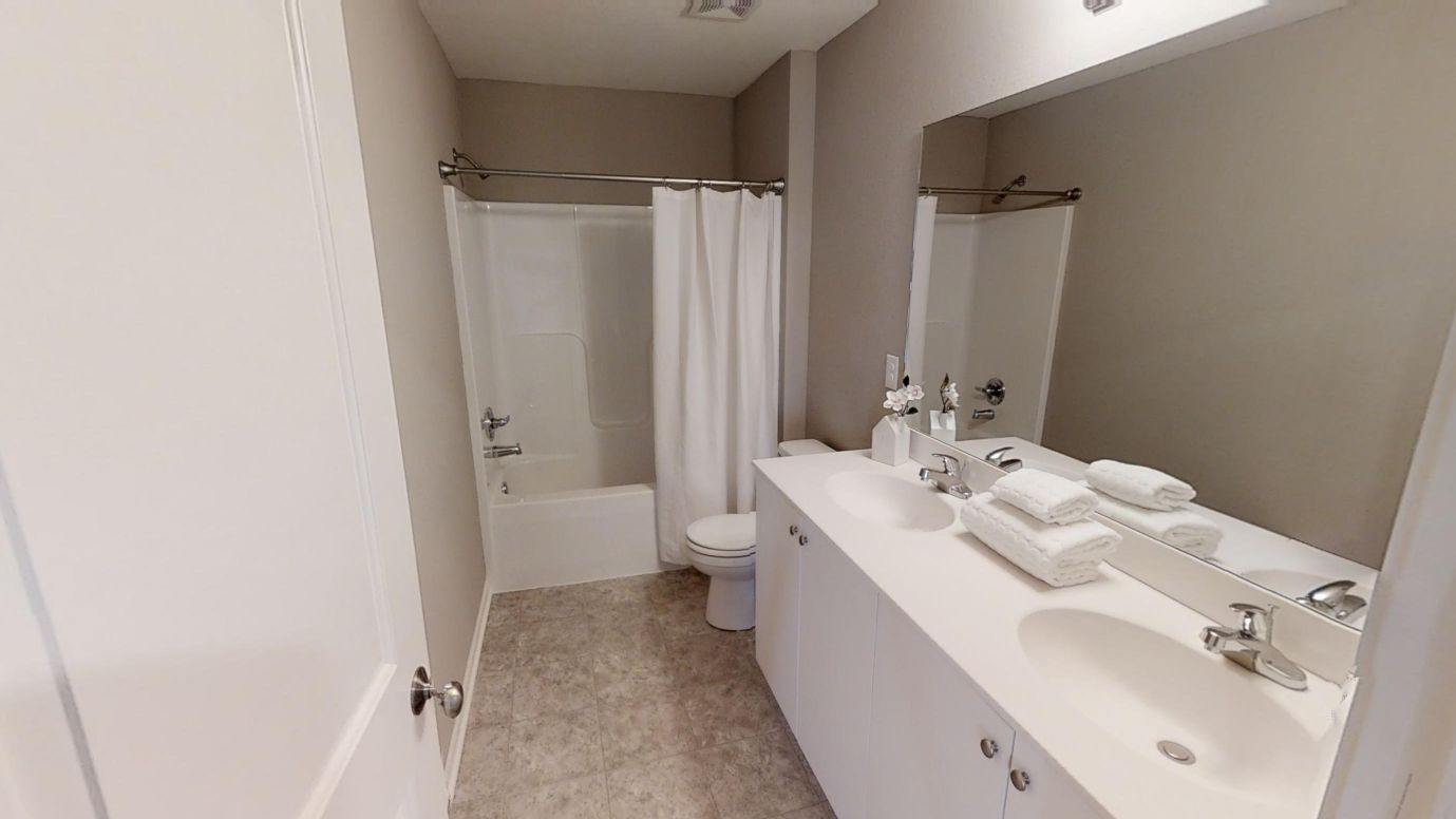 A white bathroom with a sink, mirror, toilet, and shower.